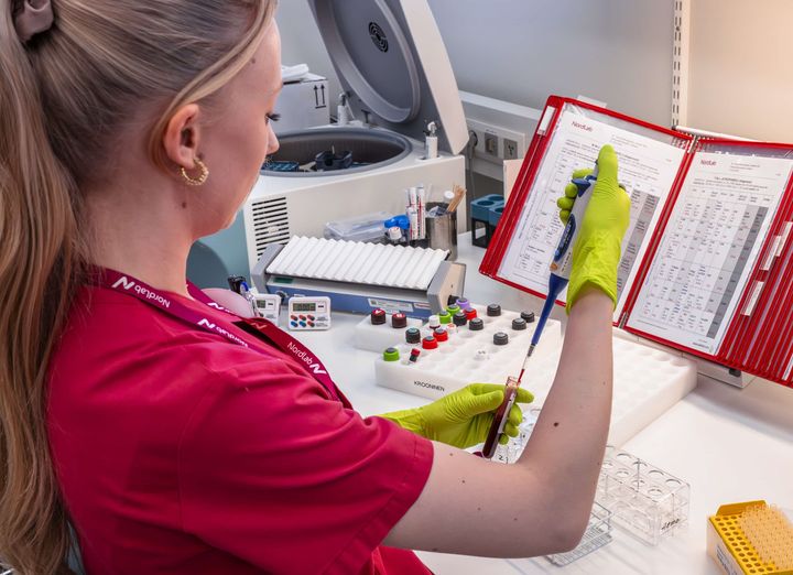 Henkilö laboratoriossa käsittelee pipettiä suojakäsineet kädessä.