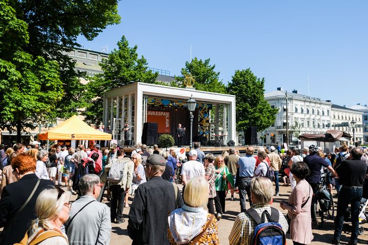 Kuvassa Espan lava, jolla seisoo pormestari Juhana Vartiainen. Lavan edessä paljon ihmisiä. Taivas on sininen ja tunnelma kesäinen.