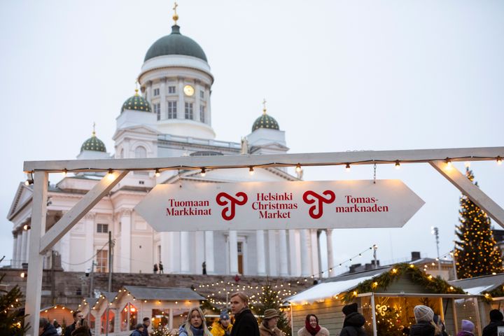 Alt-teksti: Ihmiset tutustuvat Tuomaan Markkinoihin Helsingin Tuomiokirkon edustalla talvisessa säässä. Markkinoiden kojut näkyvissä taustalla.