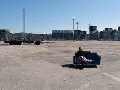 Pilvi Porkola istuu sohvalla asfalttikentällä, taustalla kerrostaloja.