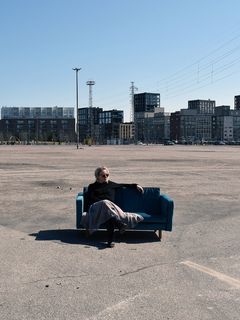 Pilvi Porkola istuu samettisohvalla asfalttikentällä, taustalla kerrostaloja.