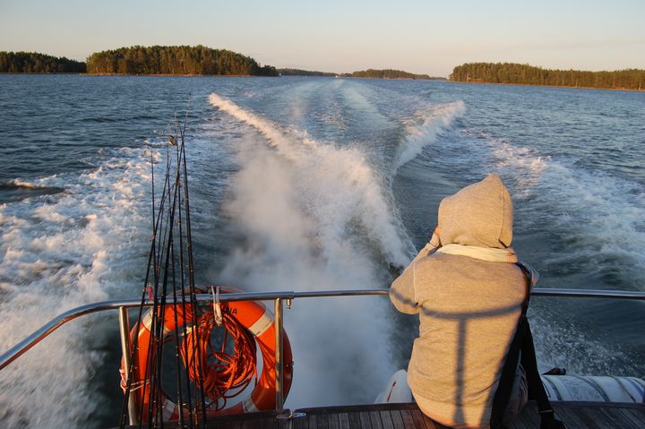 Henkilö istuu veneen takaosassa katselemassa ilta-aurinkoa merellä, ja vene jättää peräänsä vaahtovanat.