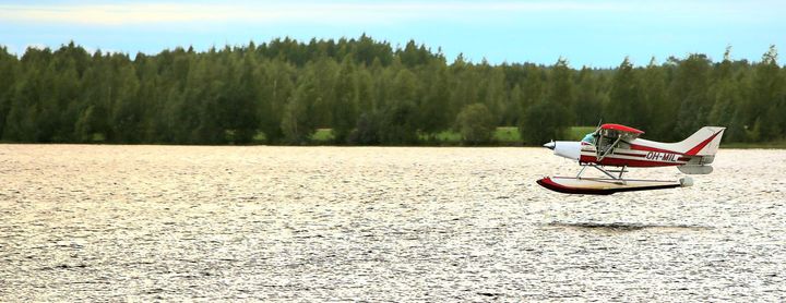 Pienlentokone laskeutuu järvelle metsämaiseman edessä.