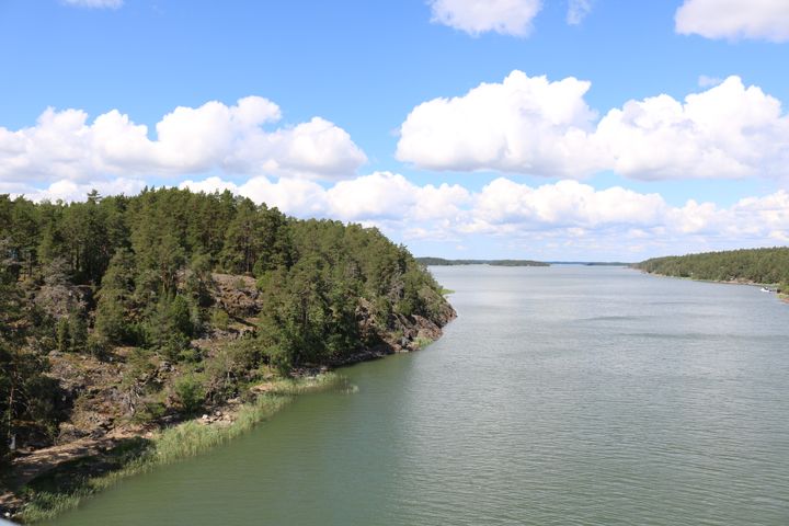 Kesäinen merimaisemakuva sillalta. Kuvassa on metsää, merta ja pilvistä taivasta.