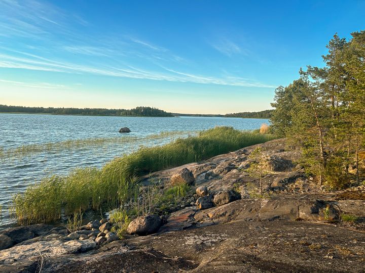 Ilta-aurinkoinen merimaisema, jossa näkyy merta ja kallioista rantaa.