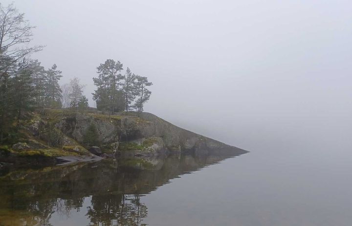 Sumuinen kallio vesistön äärellä.