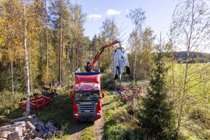 Rekka-auton lavalla oleva nosturi nostaa jätemuovia rekan lavalle syksyisessä maalaismaisemassa.