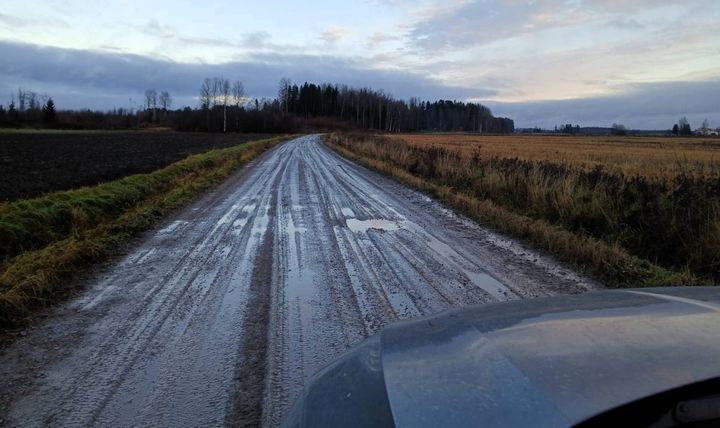 Savinen tie maaseudulla, molemmin puolin peltoja, taustalla puita ja pilvinen taivas.