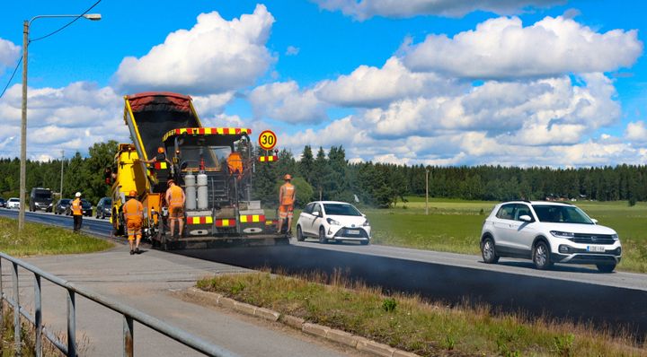 Vägarbetare asfalterar en landsväg under en solig dag, med bilar körande förbi.