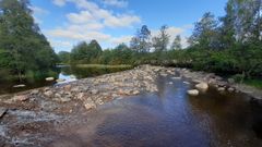 Kivinen jokiuoma, ympärillä vehreää metsää ja sininen taivas.