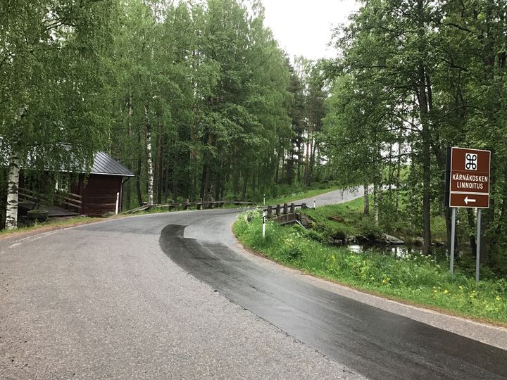 Asvalttitie kaartaa kivisillalle, jonka lähellä on  liikennemerkki Kärnäkosken linnakkeesta.