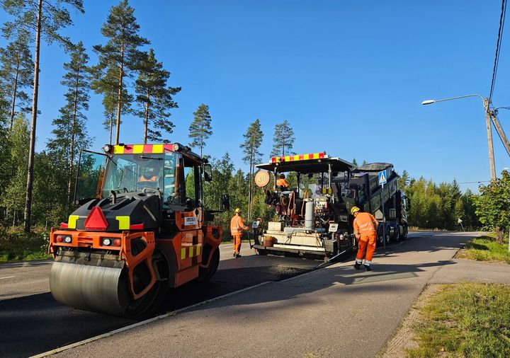 Kaksi päällystyskonetta ja kolme työntekijää asfaltoivat maantietä kirkkaana päivänä.