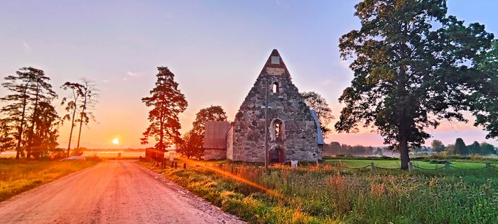 Kuva auringonlaskusta, jonka etualalla on vanhan kivikirkon rauniot ja maalaismaisema.