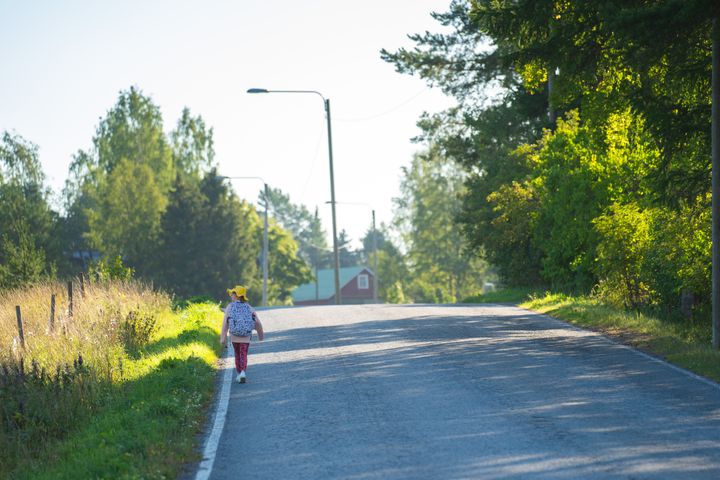 Lapsi kävelee maantien laitaa kesäisissä vaatteissa.