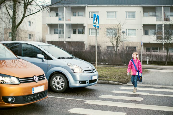 Tyttö ylittämässä suojatietä autojen edessä.