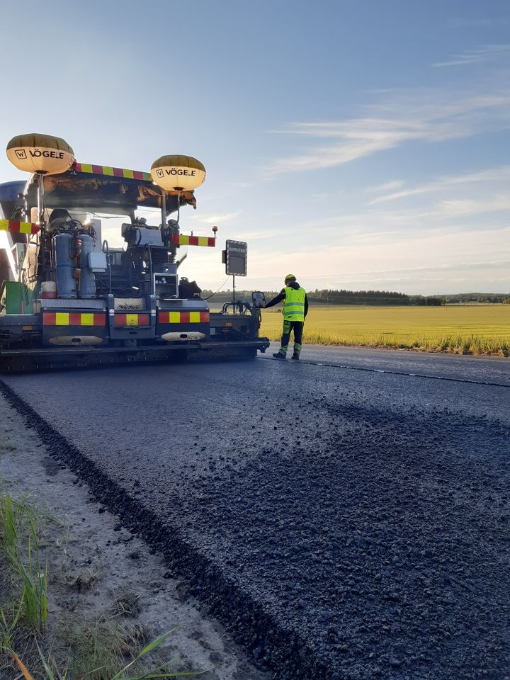 Arbetare avslutar vägbeläggningsarbete på landsbygdsväg.