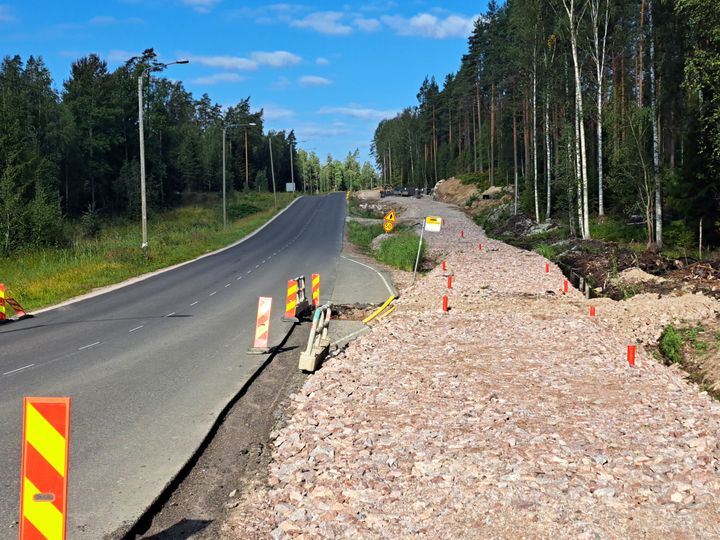 Gång- och cykelväg under konstruktion längs en landsväg, avstängd med koner.