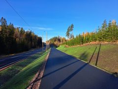 Vastapohjustettu jalankulku- ja pyörätie aurinkoisena päivänä, reunustettuna metsämaisemalla.