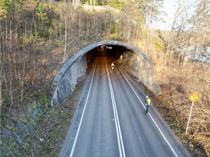 En bilväg går genom en skogstunnel i Raseborg, med trafikskyltar på sidorna.