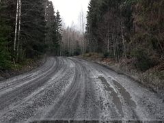 Grusväg med djupa hjulspår omgivet av skog.