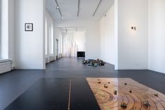 Näyttelytila, jossa lattialla on taideinstallaatioita ja seinillä ripustettuja teoksia.
