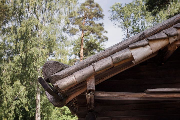 Vanhan puurakennuksen kattokulma, taustalla vihreitä puita.