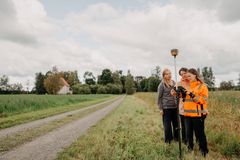 Kolme naista seisoo tien reunassa rinnakkain ja tarkastelee teknisen laitteen ruutua.