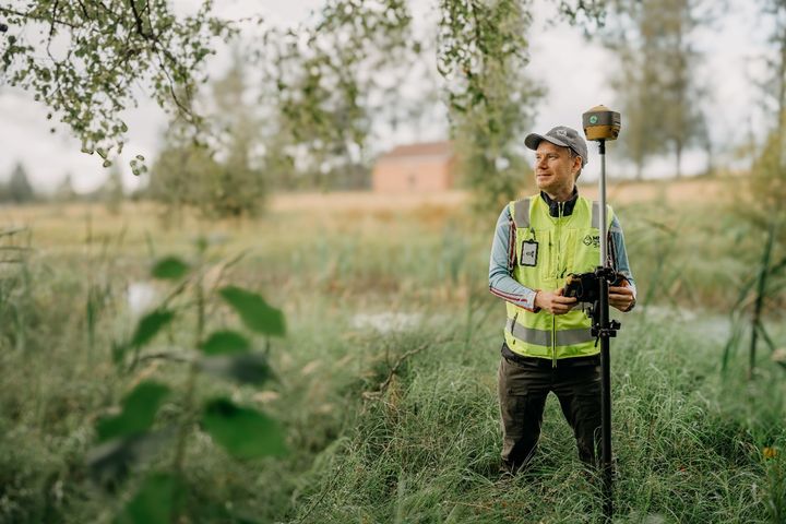 Mies seisoo pellonpientareella ja tekee maaston mittausta
