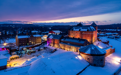 Ilmakuva talvisesta linnasta, valoilla valaistu, ympärillä luminen maisema.