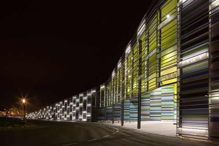 Ulkokuva Merikeskus Vellamosta, jonka julkisivu koostuu värikkäistä, valaistuista paneeleista. Näkymä on illalla, ja katuvalaistus on päällä.