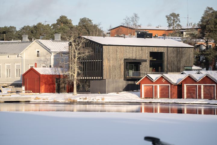 Talvisessa kuvassa keskellä näyttäytyy harmaansävyinen moderni puutalo, PAVE Studio, jossa on harjakatto ja kaksi neliönmuotoista aukkoa näkyvässä kyljessä. Rakennus asettuu joen varteen. Naapuritalona on selvästi vanhempi, yli satavuotias vaaleanharmaa harjakattoinen koulurakennus. Kuvassa näkyy myös punaisia venevajoja. Modernin rakennuksen edessä on veistoksellinen puu, vuodenajasta johtuen ilman lehtiä.