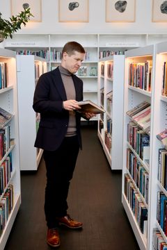 En person står och bläddrar i en bok i ett bibliotek.