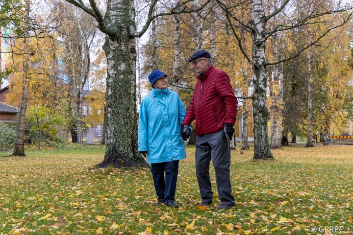 Ikääntynyt pariskunta kävelee syksyisessä puistossa värikkäiden lehtien keskellä.