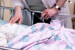 Lääkäri tarkistaa sängyssä olevaa vauvaa. Sängyssä on pinkki peitto, jossa on sinisiä norsuja.