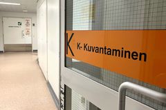 Käytävään avautuu lasiovi, jossa, oranssi teippaus ja teksti "K-Kuvantaminen".