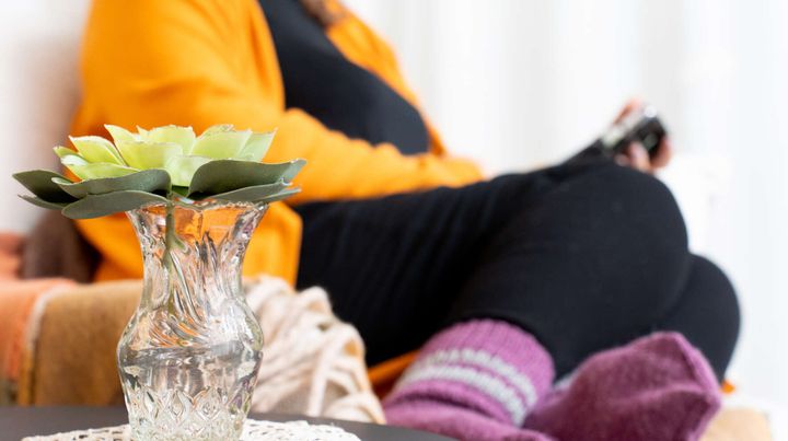 Ihminen, jolla on keltainen pusero ja viininpunaiset villasukat, istuu ja käyttää puhelinta.