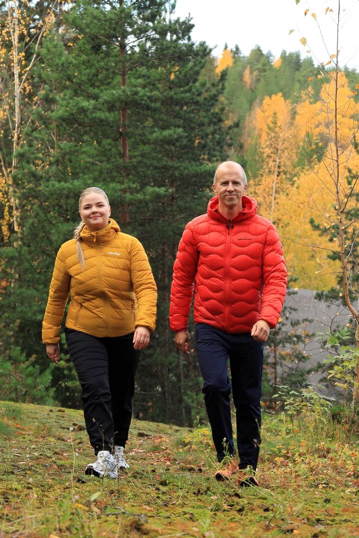 Kaksi aikuista kävelee syksyisessä metsässä värikkäissä takeissaan.