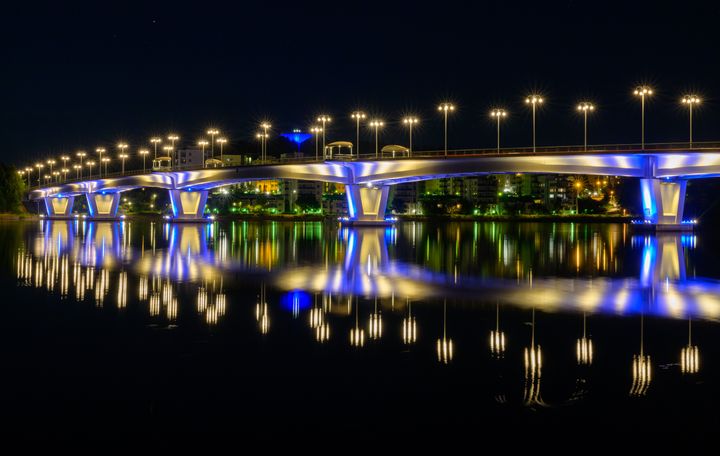 Valokuva Jyväskylässä sijaitsevasta Kuokkalan sillasta yöllä pimeässä. Sillan valot heijastuvat näyttävvästi vedenpinnasta.