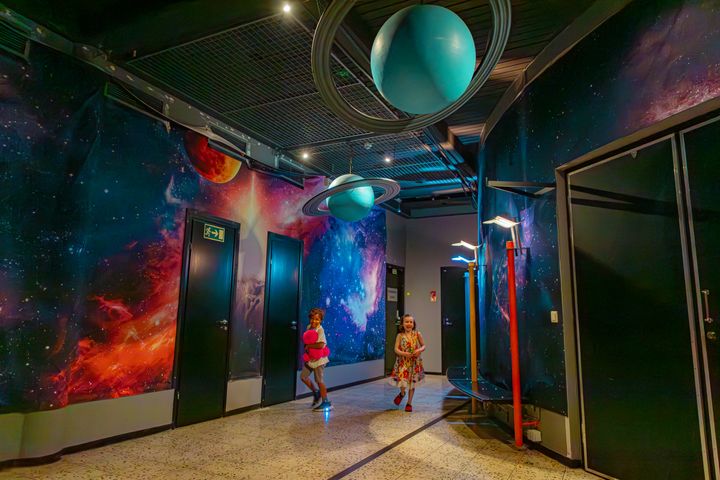 Kaksi lasta juoksee Planetaarion käytävässä tähtitaivaan ja planeettojen alla.