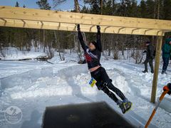 Henkilö roikkuu puisessa käsienvarassa esteradalla lumisessa maisemassa talvella.