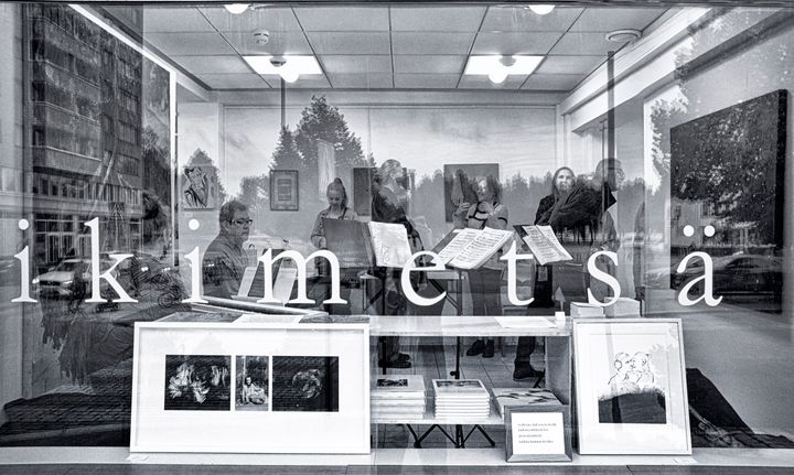 Ikimetsägallerian näyteikkunassa "ikimetsä"-teksti, sisällä ihmisiä katselemassa taideteoksia.