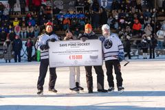 Neljä henkilöä seisoo jäällä pidellen 15 000 euron lahjoitustsekkiä Luonnonperintösäätiölle Save Pond Hockey -turnauksessa. Taustalla näkyy katsojia.