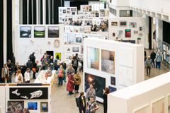 Näyttelytila täynnä ihmisiä katsomassa seinille ripustettuja taideteoksia.