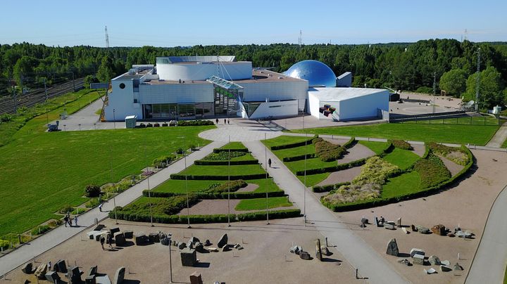 Ilmakuva Heurekan rakennuksesta, jota ympäröi vihreä maisema ja geometrisesti muotoiltu puutarha.