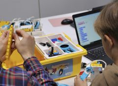 Kaksi henkilöä rakentaa robotteja LEGO-kompletilla kannettavan tietokoneen vieressä.