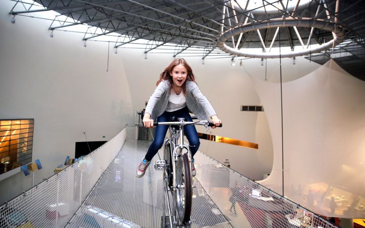 Nuori tyttö pyöräilee sisätiloissa iloisesti aidalla tai korotetulla polulla.