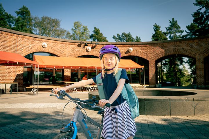 pieni koululainen polkupyöränsä kanssa ja reppu selässä Leppävaaran kirkon pihalla