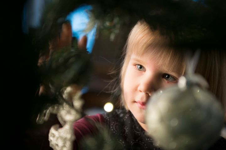 Vaaleahiuksinen pieni lapsi joulukuusen oksan takana.