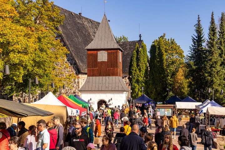 Folkmyller på marknad intill Esbo domkyrka och kyrkans klockstapel i soligt höstväder.