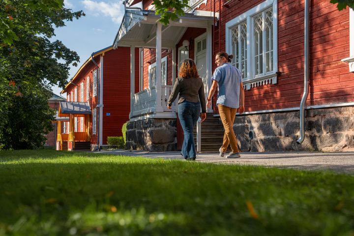 Kuvassa kaksi ihmistä kävelemässä Vaasan yliopiston Puuvilla-rakennuksen ohi.